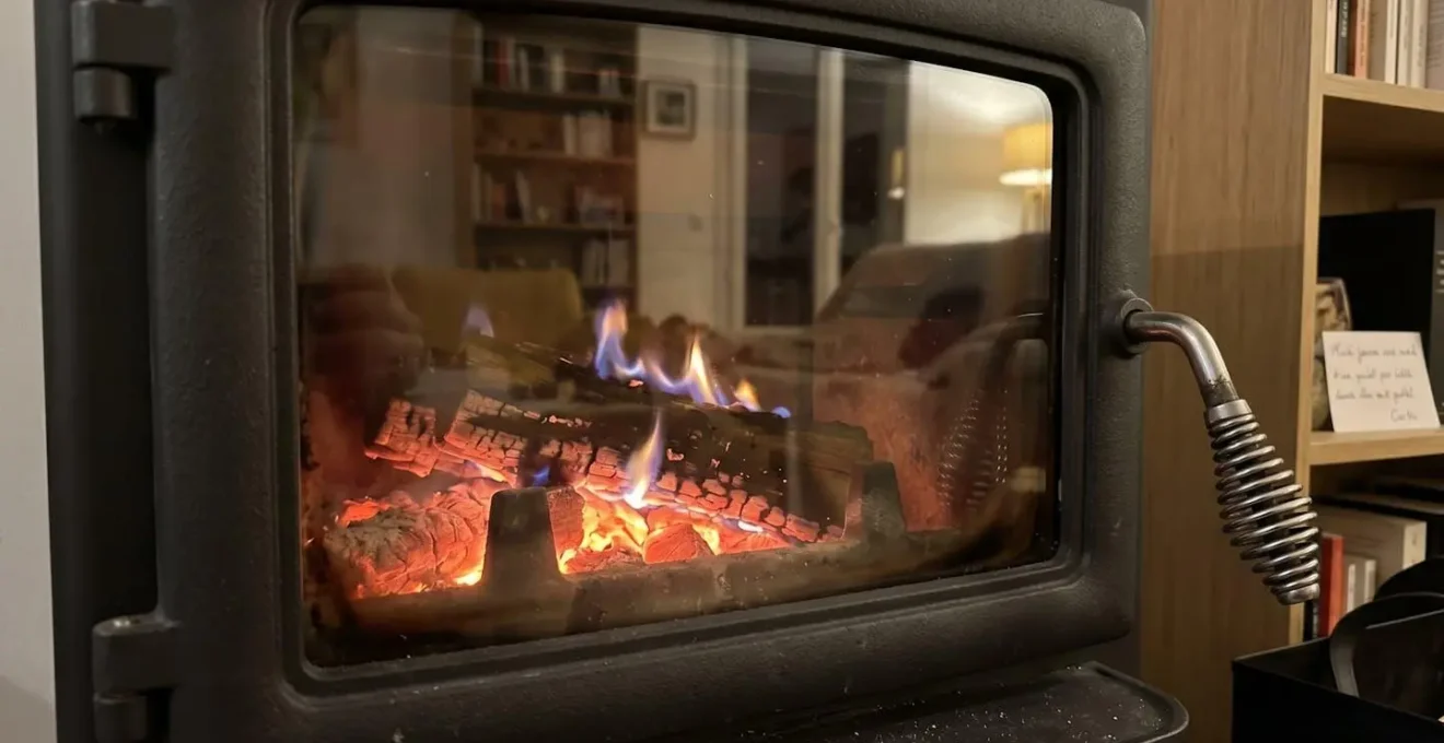 Gros plan sur la vitre d'un poêle à bois moderne montrant des braises incandescentes orangées et une flamme bleue à travers une surface transparente